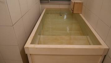 A rectangular bathtub with a glass front, surrounded by beige tiles.