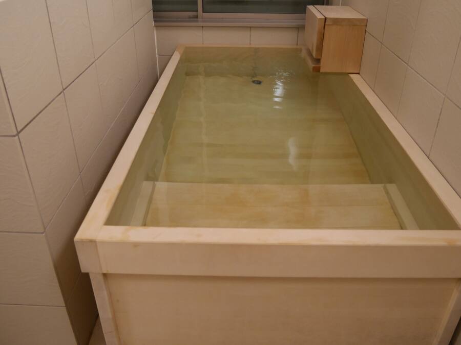 A rectangular bathtub with a glass front, surrounded by beige tiles.