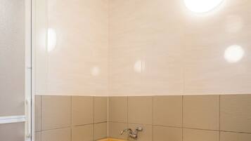 A wooden bathtub with a built-in seat, a showerhead, and a wall-mounted light fixture.