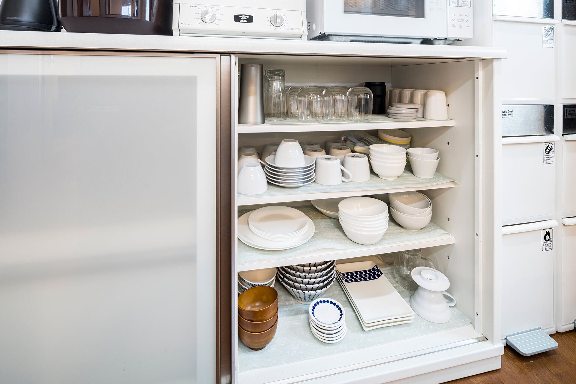A kitchen with white cabinets and a microwave above a shelf with various dishes.