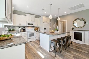 Una cocina moderna con armarios blancos, una isla central con taburetes de bar, un microondas, horno y refrigerador.