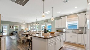 Une cuisine spacieuse avec des meubles blancs, un grand îlot central et des luminaires suspendus.