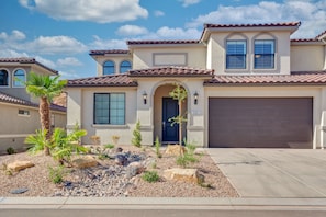 A two-story house with a garage, a front door, and a landscaped front yard with rocks and plants.