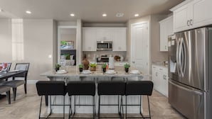 Una cocina moderna con armarios blancos, un refrigerador de acero inoxidable y una isla central con taburetes de bar.