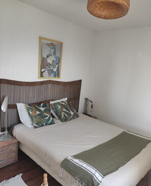 Un dormitorio ordenado con cama, almohadas, lámpara de noche, un cuadro en la pared y una lámpara colgante.