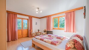 A bedroom with a wooden bed, two windows with curtains, a small table, and a chair. - Sunny holiday home with open views (Westendorf)