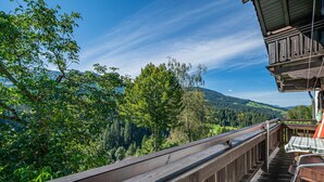 A wooden deck with a view of a forested valley and distant mountains. - Sunny holiday home with open views (Westendorf)