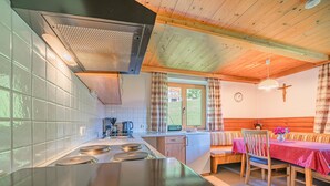 A kitchen with a stove, sink, and window. There is a dining area with a table and chairs. - Sunny holiday home with open views (Westendorf)