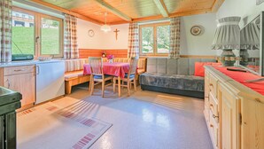 A cozy room with a wooden ceiling, a dining table with chairs, a sofa, and a kitchen area with cabinets and a sink. - Sunny holiday home with open views (Westendorf)