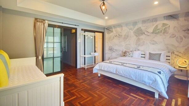 Une chambre avec un plancher en bois, un lit recouvert d’une couvre-lit à motifs, une table de chevet avec une lampe et une armoire.