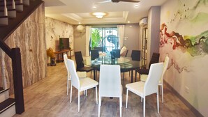 Un espace repas moderne avec une table en verre et des chaises blanches, un escalier et une fresque murale.