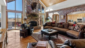 A spacious living room with a stone fireplace, leather furniture, and large windows offering a view of the outdoors. - Gorgeous Estate Home on 186 Acre Ranch only minutes from Colorado Springs or AFA (Colorado Springs)