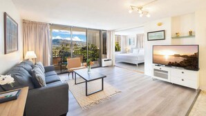 Un salon moderne avec un canapé, une table basse, un téléviseur et un balcon offrant une vue sur la ville.