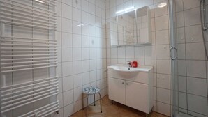 Une salle de bain avec des murs carrelés de blanc, un lavabo avec un miroir au-dessus, une douche et un radiateur.