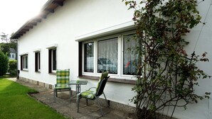 Un bâtiment blanc avec une véranda dotée de fenêtres, deux chaises et une petite table.