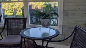 En overdækket terrasse med et rundt glasbord og to fletstole.