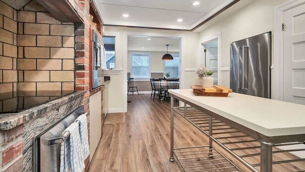 A kitchen with a brick backsplash, stainless steel appliances, a long counter, and a dining area in the background. - Magnificent Ferncrest - Towering Home on the Coast (Groton)