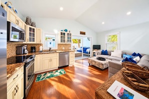 A modern kitchen with a central island, a dining area with a sofa and coffee table, and a living room with a television. - Runaway Bills (Key West)