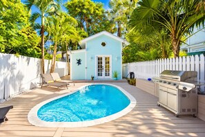 A backyard with a swimming pool, a barbecue grill, lounge chairs, and a small house.