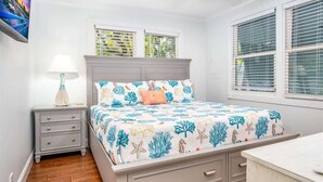 A bedroom with a bed, nightstand, dresser, and a window with blinds. - Runaway Bills (Key West)