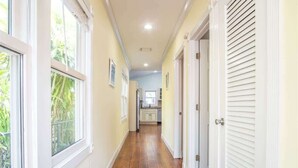 A hallway with wooden flooring, white walls, and doors leading to a kitchen area. - Runaway Bills (Key West)