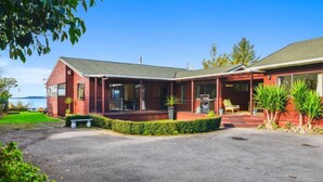 A two-story house with a covered porch, a garage, and a well-maintained lawn. - Front Row on the Lake | Jetty, Kayaks & Room to Spread Out (Rotorua)