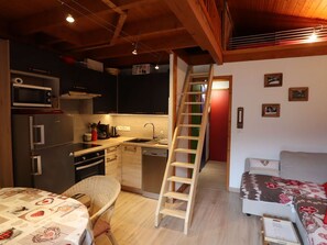 Une cuisine compacte dotée d’appareils électroménagers modernes, d’une échelle en bois, d’un coin repas avec une table et d’un canapé.