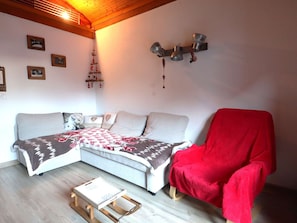 A cozy living room with a sofa, a red chair, a small wooden table, and wall decorations.