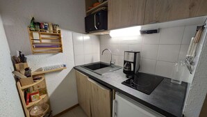 A compact kitchen with a sink, coffee maker, and wooden cabinets.