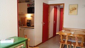 A compact kitchen with a microwave, coffee maker, and a dishwasher. There is a dining area with a wooden table and chairs.