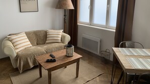 A living room with a sofa, a coffee table, a lamp, a radiator, and a window with curtains.