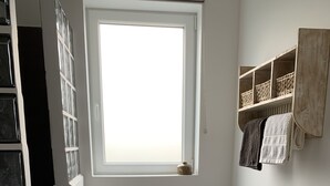 A narrow hallway with a wooden chair, a small window, and a shelf with baskets.