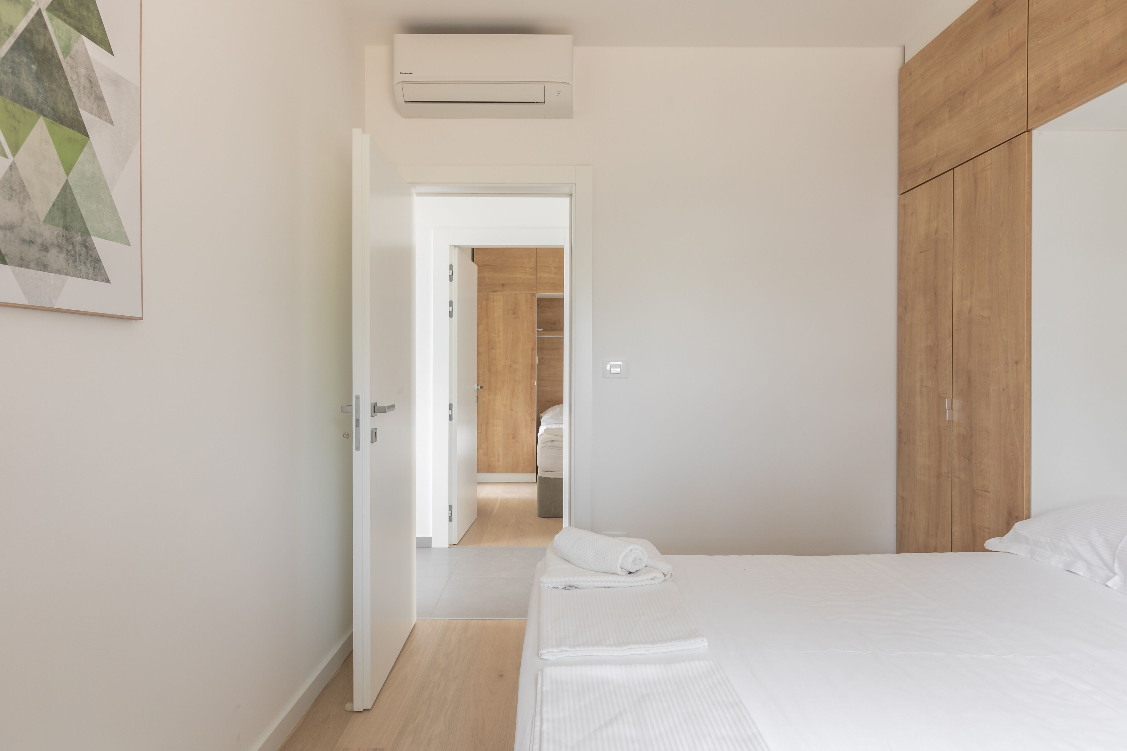 A bedroom with a bed, a wooden wardrobe, and a hallway leading to a bathroom.