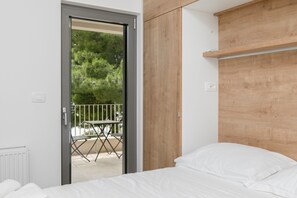 A bedroom with a bed, wooden headboard, and a door leading to an outdoor area with a table and chairs. - Villa MT Brela (Brela)