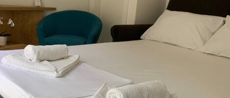 A hotel room with a bed, a teal chair, a wooden dresser, and a painting on the wall.