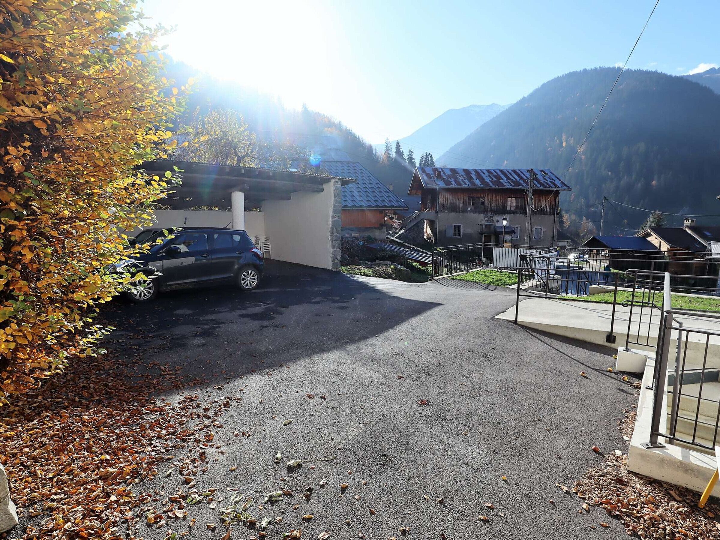 Un espace de stationnement avec une voiture, un bâtiment doté d’un toit en pente et une montagne en arrière-plan.