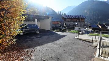 Un espace de stationnement avec une voiture, un bâtiment doté d’un toit en pente et une montagne en arrière-plan.