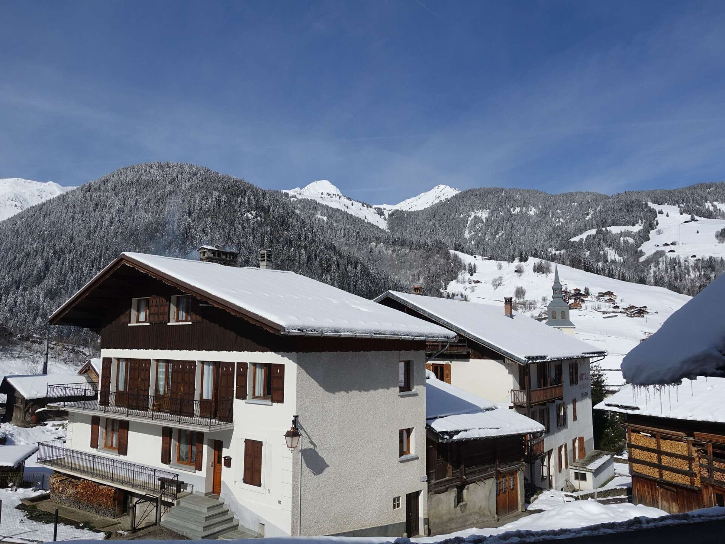 Un chalet à deux étages doté d’un balcon, d’une façade en bois et d’un toit recouvert de neige.
