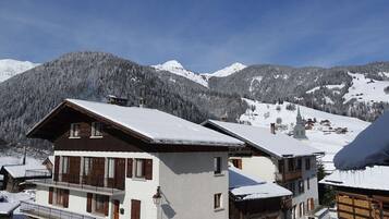 Un chalet à deux étages doté d’un balcon, d’une façade en bois et d’un toit recouvert de neige.
