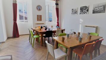 Un coin repas avec une table et des chaises en bois, une horloge et une vue sur la mer par de grandes fenêtres.