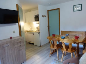 A compact kitchen with a dishwasher, oven, and a dining area with wooden chairs and a table.