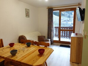 A dining area with a wooden table and chairs, a sofa, and a view of a snowy landscape through a glass door.