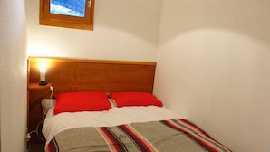 Una habitación pequeña con cama, mesita de noche, lámpara y ventana con vistas a un paisaje nevado.