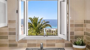 A bathroom with a window offering a view of the ocean and palm trees. - Apartamento Buganvilla - Increíbles vistas al mar (San Jaime Mediterráneo)