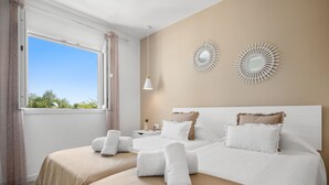 A hotel room with two beds, a large window with curtains, and decorative wall art. - Apartamento Buganvilla - Increíbles vistas al mar (San Jaime Mediterráneo)