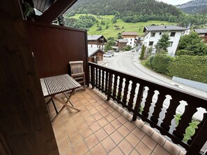 A balcony with a view of a rural road and houses, a wooden chair, and a tiled floor.
