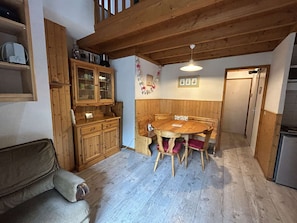 A dining area with a wooden table and chairs, a wooden cabinet with glass doors, and a ceiling with exposed beams.