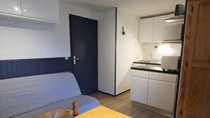 A compact room with a bed, a wooden table, a kitchenette with a stove, and a door. - Cozy 4/5 Pers Apartment with Balcony, Pool Access & Close to Ski - 2 Stars (Arêches-Beaufort)