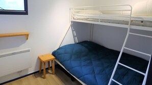 A bunk bed with a blue mattress, a small wooden stool, a white radiator, and a window with blinds. - Cozy 4/5 Pers Apartment with Balcony, Pool Access & Close to Ski - 2 Stars (Arêches-Beaufort)
