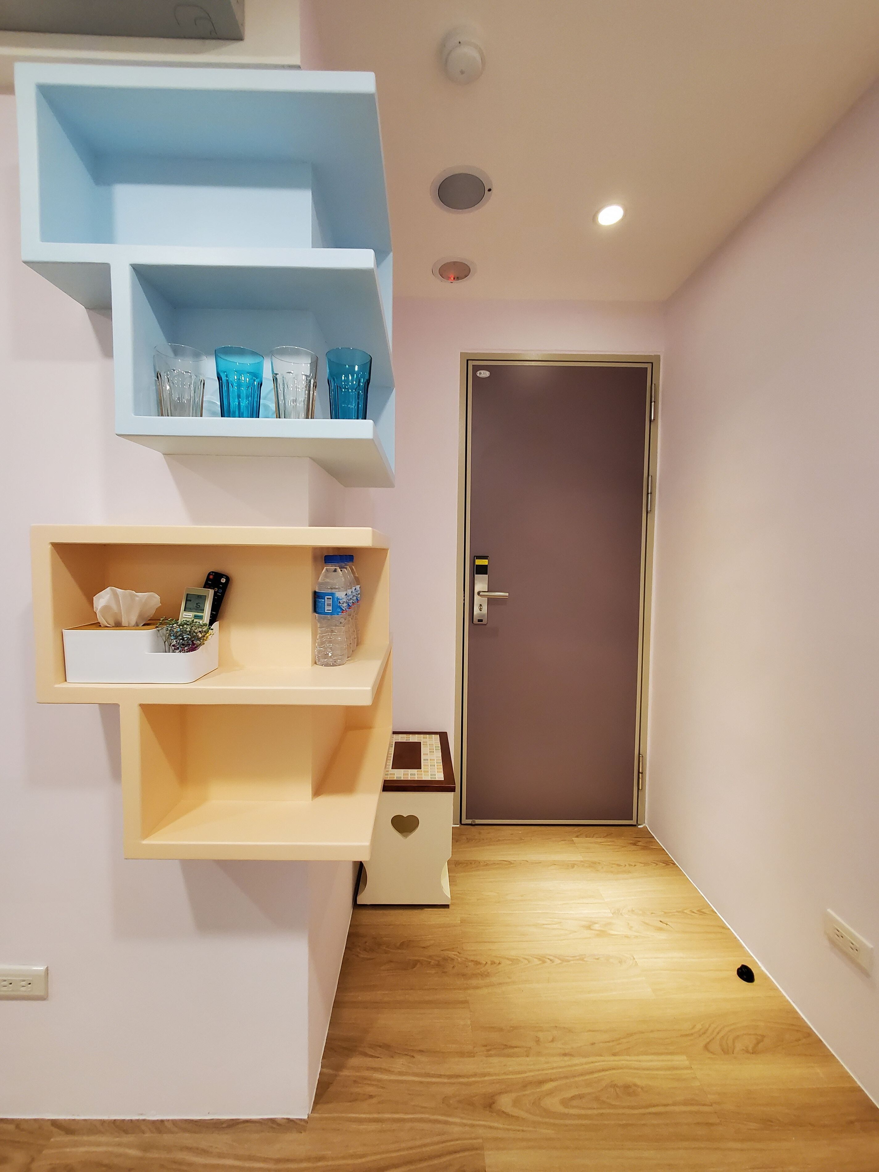 A hallway with a wooden floor, a door, and two white shelves with various items.